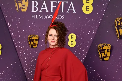 Getty Images Maggie O'Farrell con un vestido rojo y un tocado de plumas rojas